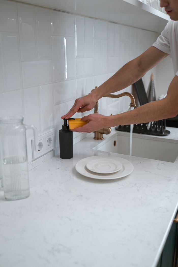 services-01 Close-up of hands washing dishes at a modern kitchen sink with white counter.